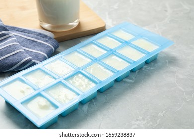 Ice Cube Tray With Frozen Milk On Grey Table