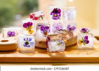 Ice cubes with flowers violets on wooden table.