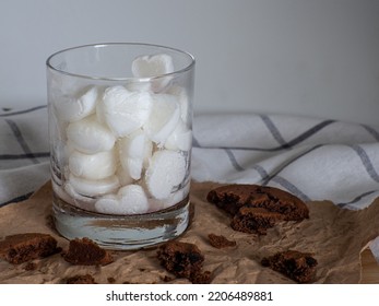 Ice cubes made from milk in heart shape in glass. Space for text. Cocoa cookies with pieces of chocolate inside on a baking paper on a white background. Valentines day breakfast eating, love concept. - Shutterstock ID 2206489881