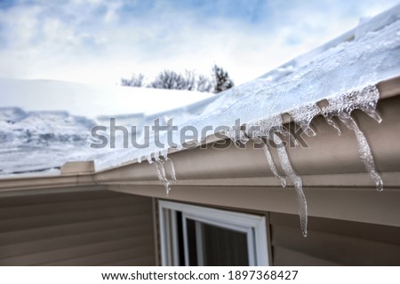 Ice dam in gutter and ice frozen on roof in winter, shallow focus on icicles in foreground 
