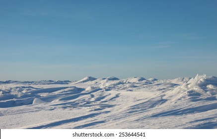 Ice desert. The ridges in the sea, snowy hills on a frozen plain and blue sky