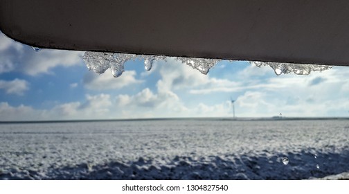 Ice drops melting from metal sign on a blue sky background with snowy fields