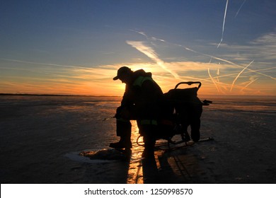  Ice Fishing Angler Silhouettes On Ice And Beautiful Yellow Sunset With Chemtrail From Airplane In Pärnu Bay, Baltic Sea, Pärnu County, Estonia