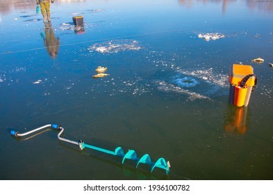 Ice Fishing Auger And Fisherman Sitting In The Background On The Ice