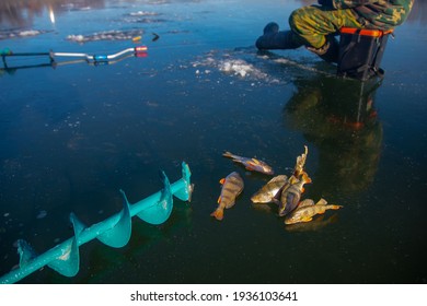 Ice Fishing Auger And Fisherman Sitting In The Background On The Ice