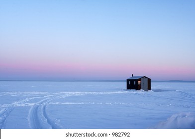 Ice Fishing Hut On A Frozen Lake During Sunrise.