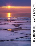 Ice floes float on Lake Superior during a winter thaw. A rising sun breaks the horizon and cast light and reflections across the water and ice on a cold winter morning