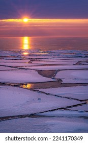 Ice floes float on Lake Superior during a winter thaw. A rising sun breaks the horizon and cast light and reflections across the water and ice on a cold winter morning - Shutterstock ID 2241170349