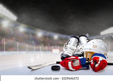 Ice Hockey Helmet, Skates, Gloves, Stick And Puck In Brightly Lit Outdoor Stadium With Focus On Foreground And Shallow Depth Of Field On Background. Deliberate Lens Flare And Copy Space.