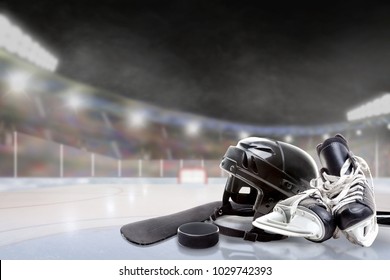 Ice hockey helmet, skates, stick and puck in brightly lit outdoor stadium with focus on foreground and shallow depth of field on background. Deliberate lens flare and copy space.
