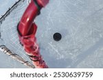 An ice hockey puck in the goal, on textured ice with skate tracks.