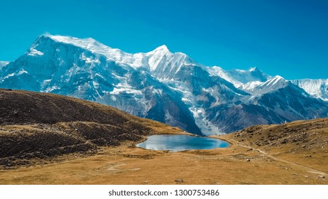 Ice lake, as part of the Annapurna Circuit Trek detour, Himalayas, Nepal. Annapurna chain in the back, covered with snow. Clear weather, dry grass, snowy peaks. Freedom, solitude, chill and relaxation