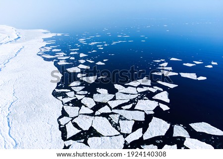 Ice melting in blue sea water, view from above photographed by drone