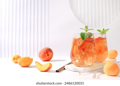 Ice peach tea or cocktail with mint and apricots, a recipe for a refreshing summer drink. Two glasses with peach fruit lemonade on light table, detox diet and weight loss concept, menu for restaurant