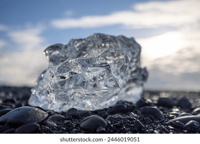 Ice is rests upon a cluster of rocks at the shoreline, contrasting the blue sky overhead. The solid bedrock meets the fluidity of the icy mass. Diamond Beach, Iceland - Powered by Shutterstock