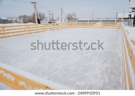 Ice rink outside in cold winter weather, empty ice field, wooden fence on ice rink, rustic playground for winter games. High quality photo