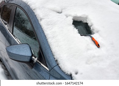 Ice Scraper Tool For Clearing Automobile Is On The Hood Of The Car. Snow Removing From Car After Blizzard. Snowfall In The City.