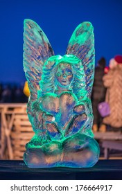 Ice Sculpture Of Woman With Wings And Heart. Colored Lights In Background