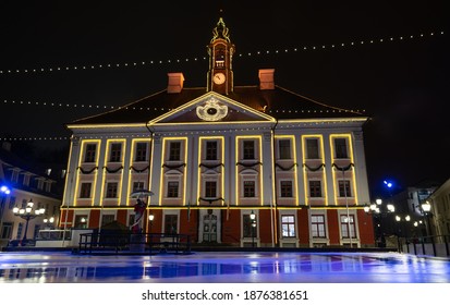 Ice skating arena built for the winter period. Colorful led lights as decorations. Empty skating field -just cleaned-wet.Old historical building. Amazing reflection Tartu town halls main square