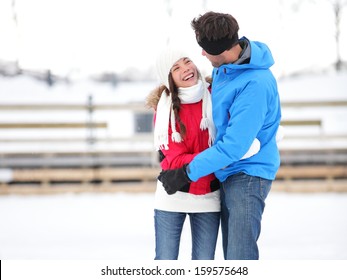 Ice Skating Romantic Couple On Date Iceskating Embracing. Young Couple Holding Hands On Ice Skates Outdoors On Open Air Rink In Snowy Winter Landscape. Multiracial Couple, Asian Woman, Caucasian Man