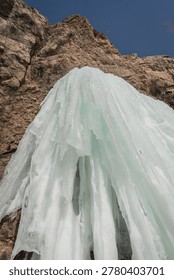 Ice structure flows down a rugged cliff, highlighting the unique formations of frozen water against a bright blue sky