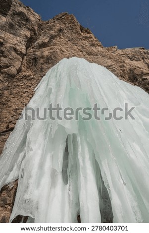 Ice structure flows down a rugged cliff, highlighting the unique formations of frozen water against a bright blue sky
