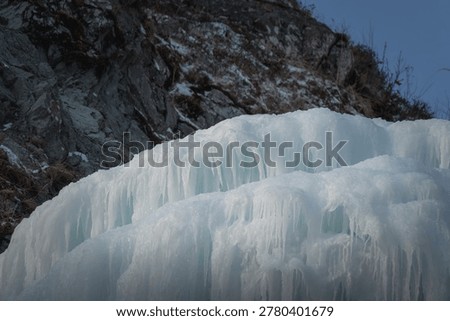 Ice structure on a rocky surface displays detailed textures and patterns under a clear blue sky, highlighting the beauty of winter in a natural setting