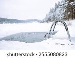 Ice swimming place. Bright winter day with a frosted ladder leading into a natural ice swimming hole on a snow-covered lake.