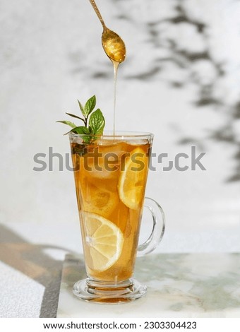 Ice tea on a tall glass with lemon and honey dropping from spoon