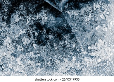 Ice texture background. The textured cold frosty surface of the ice with cracks on the dark blue background.