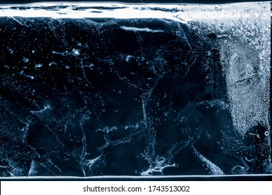 Ice Texture Blue Toned Background. Textured Frosty Surface Of Thick Ice Block With Air Bubbles On Black Background.