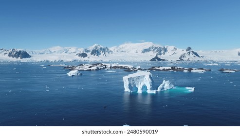 Iceberg drift in Antarctica ocean bay dark blue sea. The massive ice formation floats majestically in cold water. Mountain range in background. Sunny day. Expeditions and adventures. Aerial drone view - Powered by Shutterstock