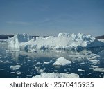 Iceberg floats in the deep blue waters of the icefjord near the Eqip Sermia Glacier in Greenland, with distant snow-capped mountains under a clear sky