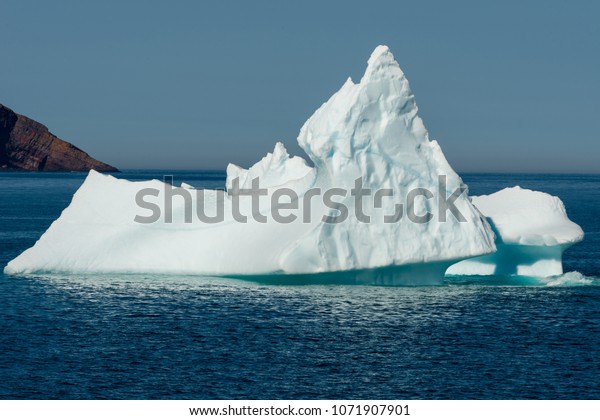 An iceberg grounded in the bay. The ocean
is deep blue under a pale blue sky. There's land in the left and a
horizon dividing the ocean from the
sky.