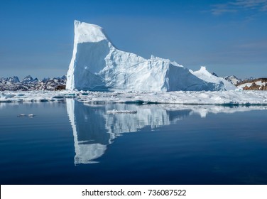 An iceberg reflect in the arctic sea in front of the coast of Greenland in white and blue colors - Powered by Shutterstock