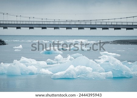 Icebergs can be seen floating in the iceberg lagoon under a bridge, creating a stunning natural landscape with the polar ice cap in the background. Iceland