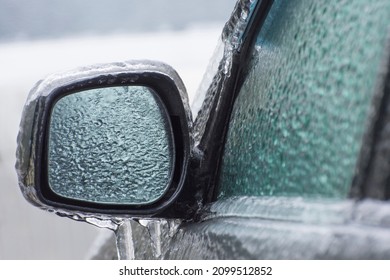 Ice-covered car mirror with icicles, glass and side doors. Icing vehicle on a winter day after freezing rain in Ukraine. Blurred background. - Shutterstock ID 2099512852