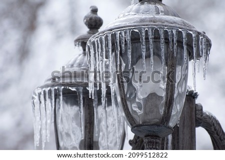 Ice-covered street light with icicles, close up. Icing  city park on a winter day after freezing rain in Mykolaiv. Blurred background.