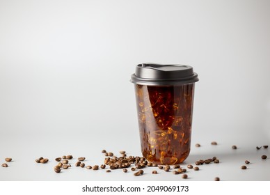 Iced Americano Coffee With Coffee Beans On Grey Background. Black Coffee Package For Takeaway. Cold Beverage Product.