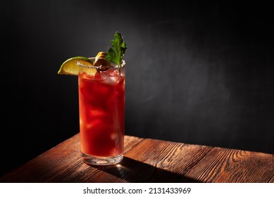 Iced bloody Mary (Caesar) cocktail  in a glass, rimmed by salt and pepper on a wooden bar and dark background. Horizontal photo with shallow depth of field and copyspace.   