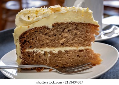 Iced Carrot Cake Topped With Cream And Coconut, Served On A Plate With A Fork. Close Up View.