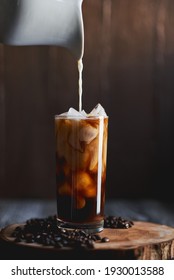 Iced Coffee With Creamer Being Poured Over Ice. Wooden Background. 