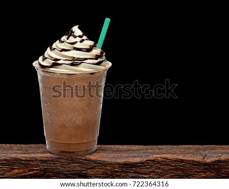 Iced coffee or frappuccino with cream in takeaway disposable cup on wooden table with black background.