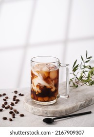 Iced coffee in a glass with cream, ice cubes and grains on a light marble background with morning shadows. The concept of a cold summer drink. Copy space. - Shutterstock ID 2167909307