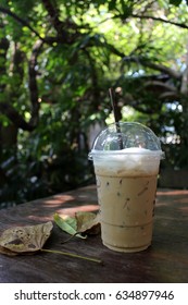 Iced coffee on a table with fallen leaves in a sunny tropical garden in Asia
