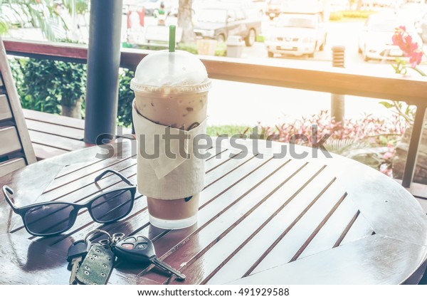 iced coffee in plastic cup, glasses\
and car keys on wooden table, travel concept. vintage\
tone