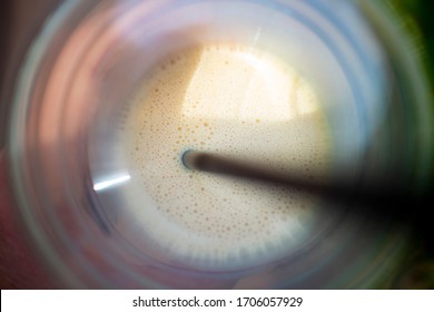 Iced Coffee In A Plastic Takeaway Cup, With A Paper Straw. Angle Is Looking Down Inside Of The Cup, Showing The Bubbles And Froth On Top, As Well As The Straw. The Cup Is Blurred; Bubbles Are Sharp.