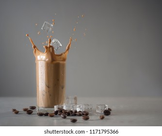 Iced Coffee Splash With Ice Cubes And Beans Against Grey Concrete