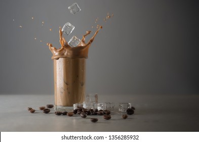 Iced Coffee Splash With Ice Cubes And Beans Against Grey Concrete