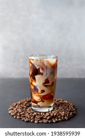 Iced Coffee In A Tall Glass With Cream And Coffee Beans Around Tumbler On Gray Background With Copy Space